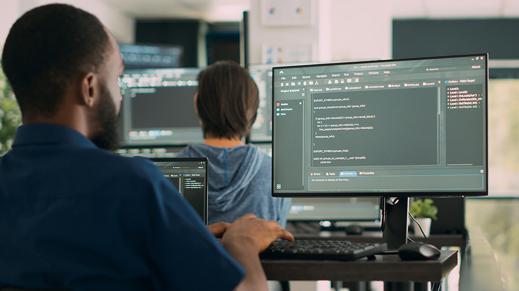 Developers working at adjacent monitors with code and IDEs open.