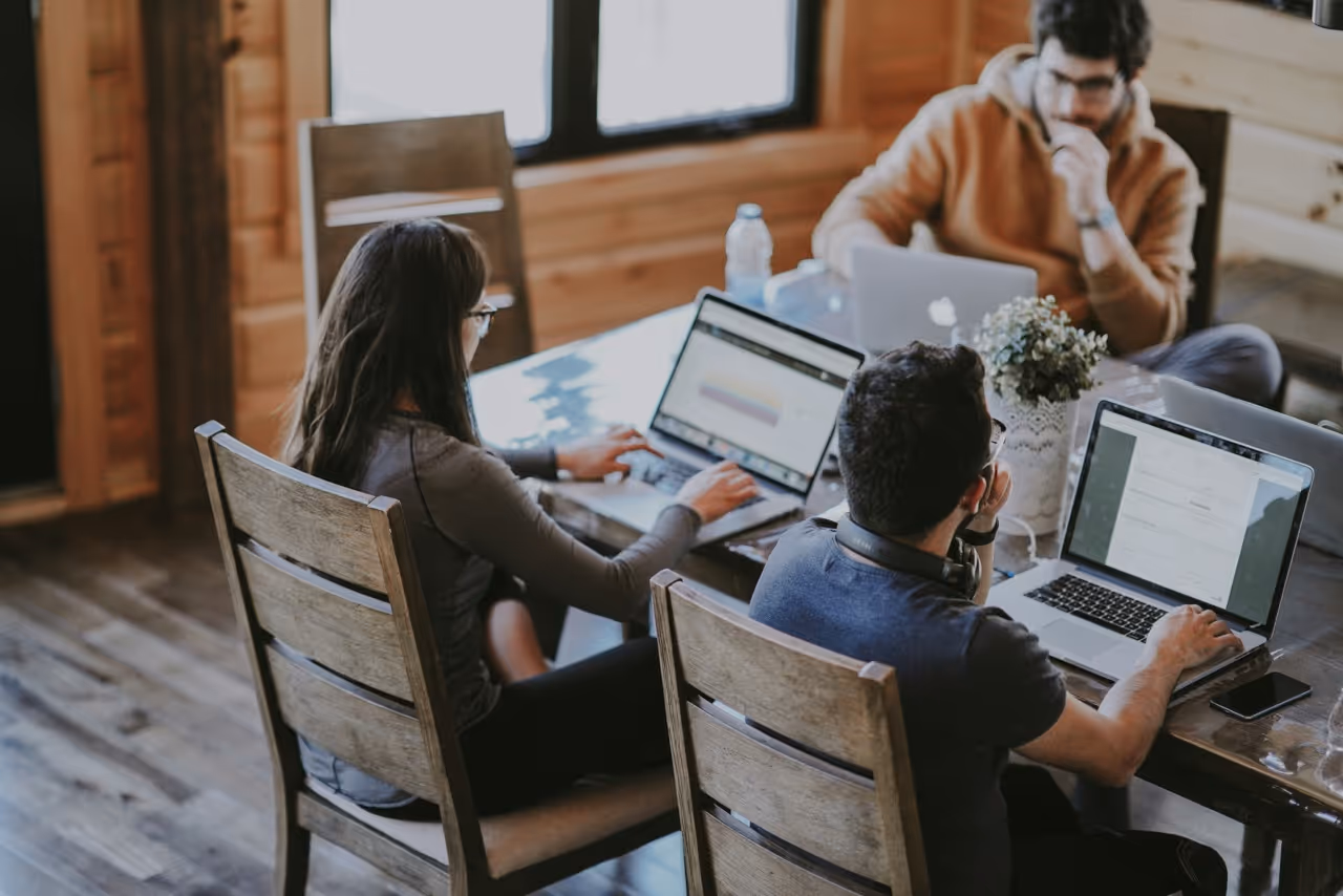 Group of people working on laptops around a shared table in a wood- panelled workspace
