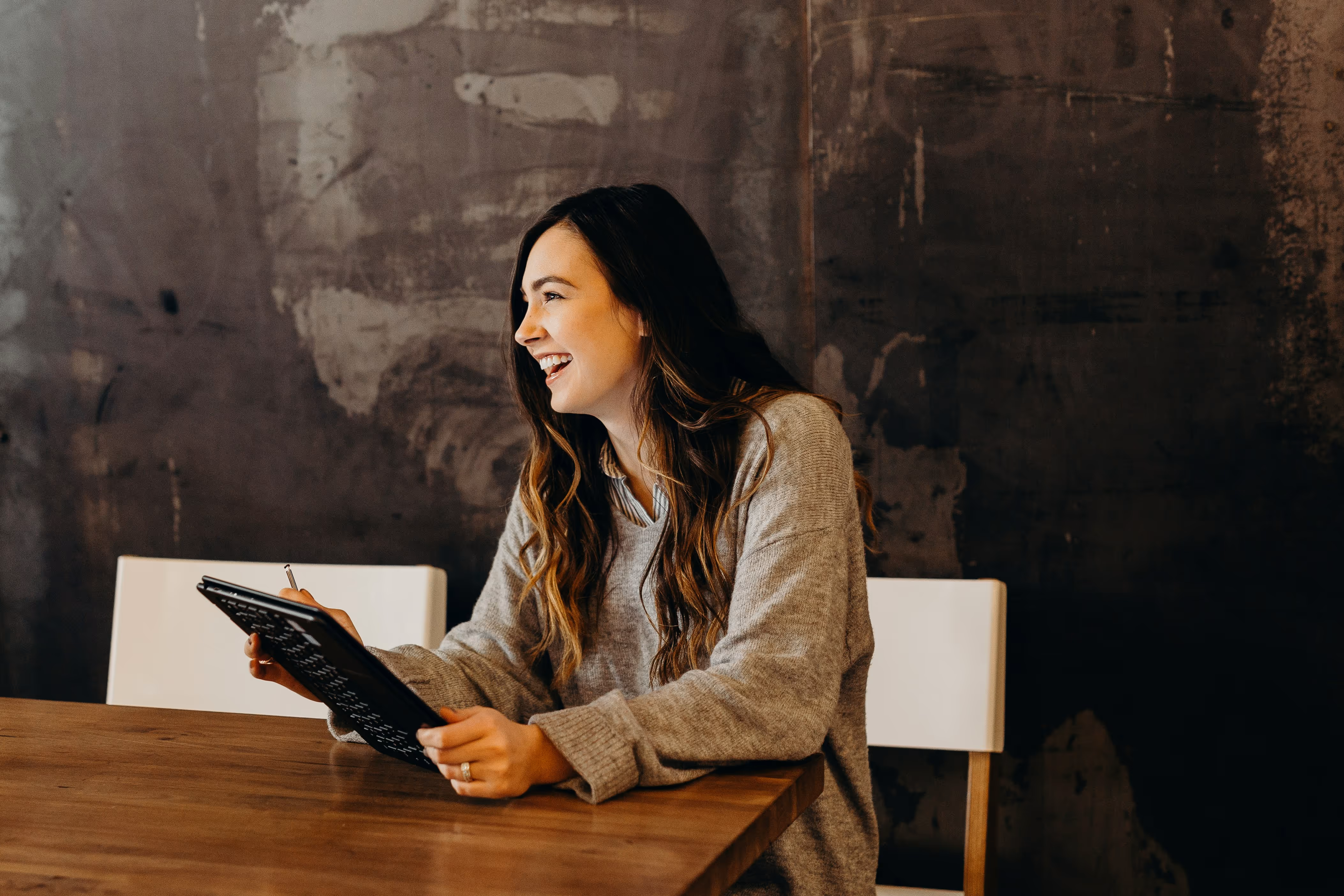 Woman smiling during a conversation, holding a tablet and stylus at a wooden table