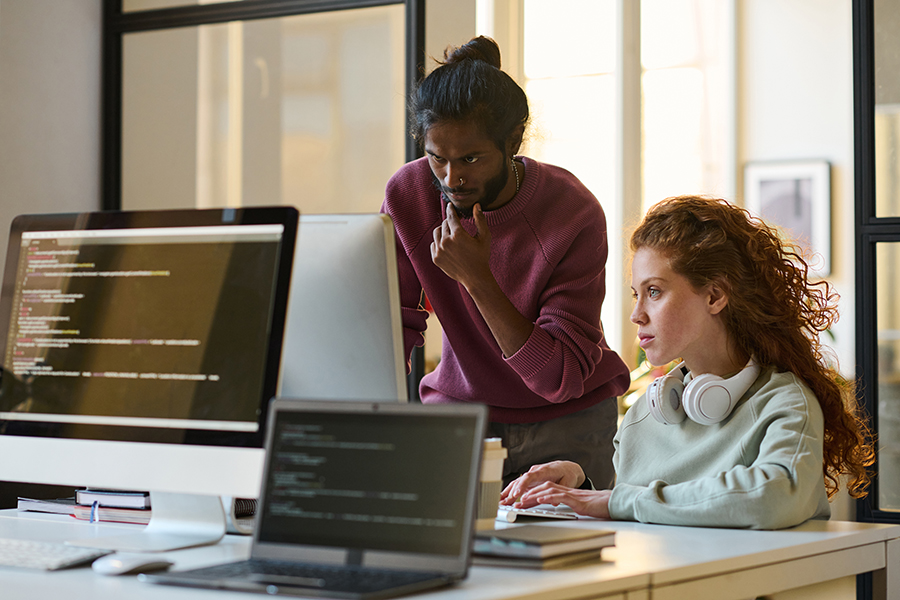 Two colleagues focused on a desktop screen in a sunlit office workspace. ABOUT US 1. Group of people working on laptops around a shared table in a wood- panelled workspace 2. Small team collaborating on laptops in a rustic meeting room with