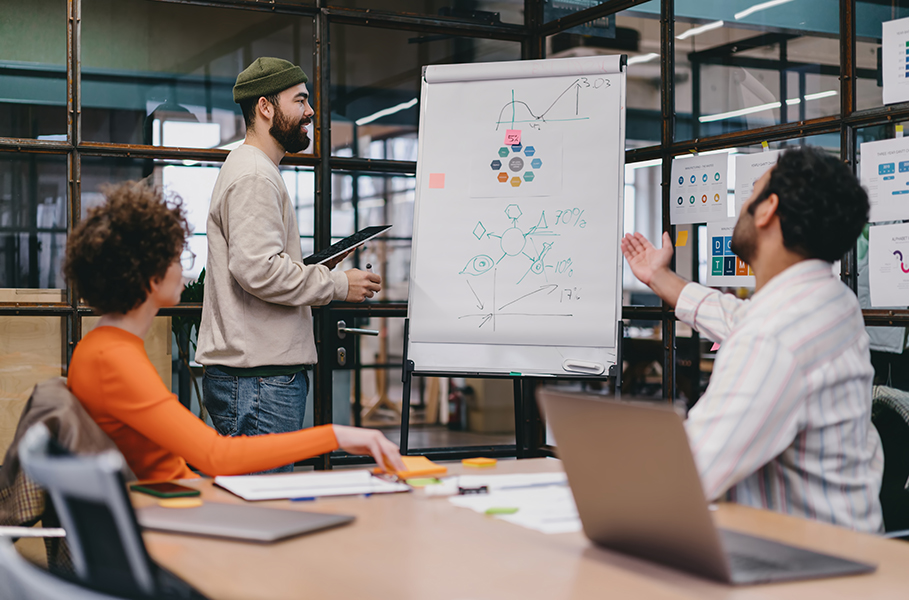 Presenter leading a whiteboard session with a team in a meeting room.