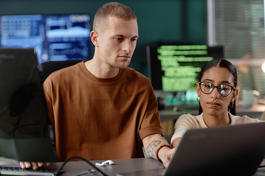 Man concentrating at a computer with blurred code on monitors behind him.