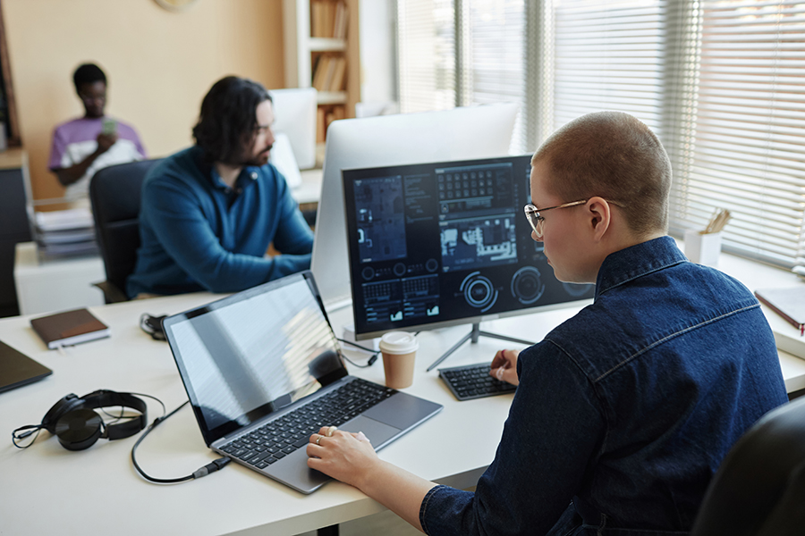 Two people reviewing dashboards and technical data on large monitors in a workspace.